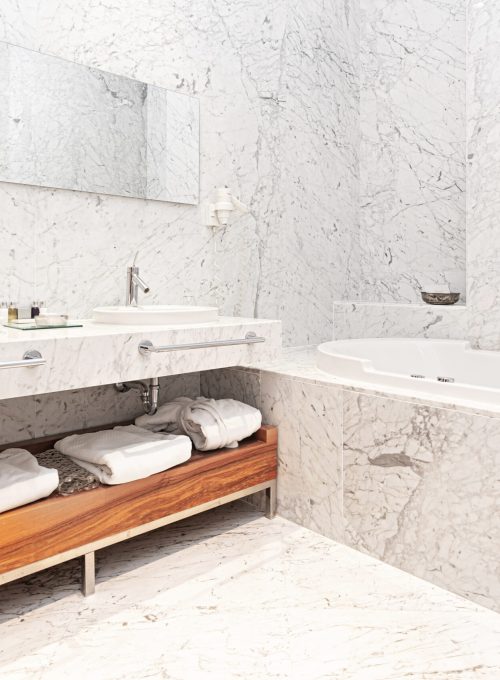 beautiful interior of a modern white marble hotel batroom with bathtube and towels.